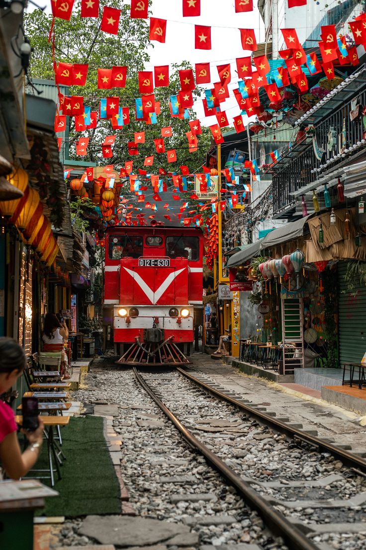 Train coming through Hanoi Train Street with Vietnamese flags overhead